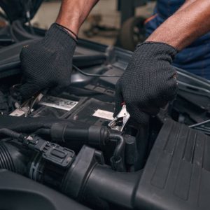 Person in car repair shop applying positive and negative clamps of battery load tester to accumulator unit