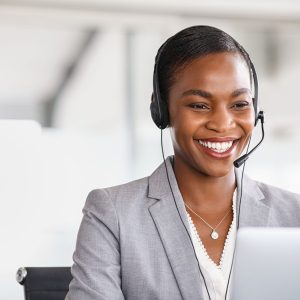 Smiling african american customer care representative working with headset in office. Beautiful black woman telemarketing agent working in call center. Call center agent with headset makinga video call with client.